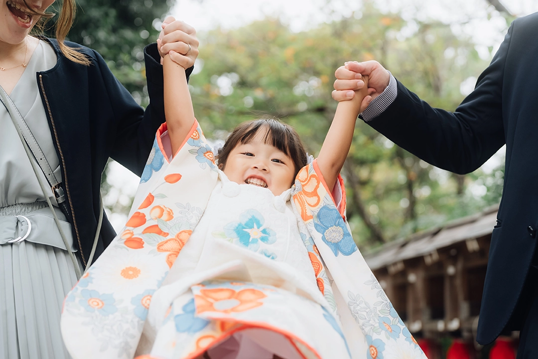 七五三の着物を着て、両親の手にぶら下がる女の子